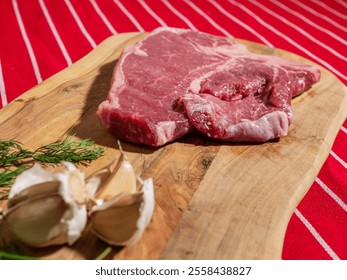 Fresh uncooked T bone steak with fresh dill and garlic cloves on wooden cutting board and on classic red and white stripe table cloth. High quality beef meat product. Butcher craft. - Powered by Shutterstock