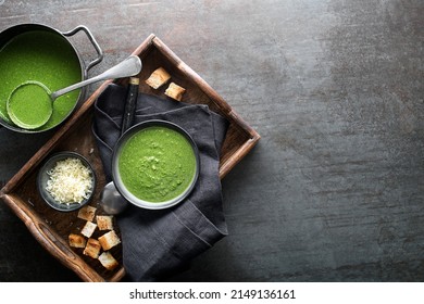 Sopa de crema de verduras fresca con queso parmesano y croutons sobre rodales de fondo gris.