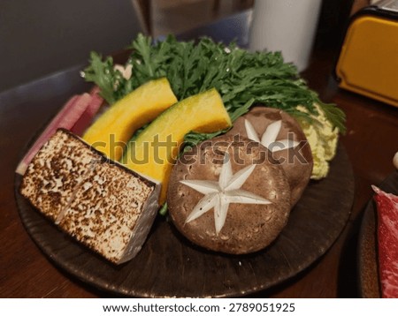 A fresh vegetable platter featuring sliced tofu, shiitake mushrooms, crown daisy leaves, baby cabbage wedges, red heart radish, and pumpkin pieces, arranged for hot pot or salad.