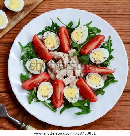 Fresh vegetable salad with chicken breast and quail eggs. Salad with tomatoes, rucola, quail eggs, chicken breast and spices on a plate and a wooden background. Healthy nutrition. Closeup. Top view