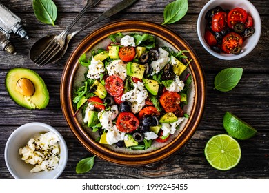 Fresh vegetable salad with mozzarella, tomatoes, avocado, lettuce, black olives and onion on wooden table  - Powered by Shutterstock