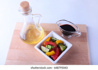 fresh vegetable salad with tomato, cucumber, bell pepper, lettuce leaf in white bowl, olive oil and balsamic souce in bottle. Selective focus.
