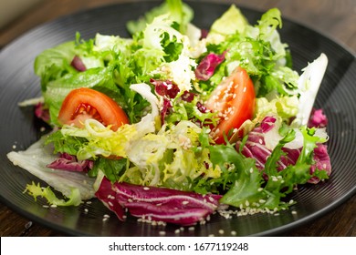 Fresh vegetable salad, tomato. the side view is very close, the structure of the salad on a dark stylish plate is distinguishable. bright appetizing colors