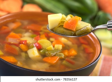 Fresh vegetable soup on spoon made of green bean, pea, carrot, potato, pepper, tomato and leek (Selective Focus, Focus on the carrot, leek and green bean on the spoon)