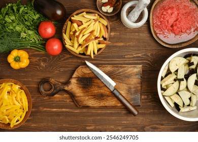 Fresh vegetables are arranged on a wooden countertop, including tomatoes, eggplants, and herbs. A sharp knife rests on a cutting board alongside bowls of chopped ingredients, ready for cooking. - Powered by Shutterstock