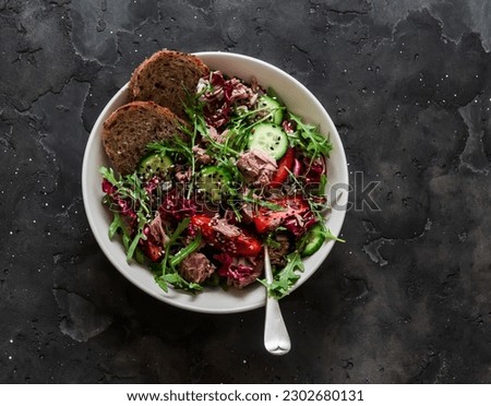 Fresh vegetables, arugula, radicchio salad with canned tuna on a dark background, top view    