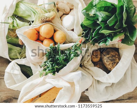 fresh vegetables in eco cotton bags on table in the kitchen. lettuce, corn, potatoes, apricots, bananas, rucola, mushrooms from market. zero waste shopping concept.   ban plastic