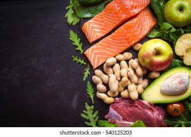 Fresh vegetables, fruits, fish, meat, nuts on black chalk board background. Cauliflower, avocado, apples, tomatoes, salmon, beef, spinach, herbs. Diet/healthy/paleo food. Ingredients. Space for text - Shutterstock ID 540125203