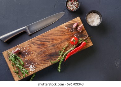 Fresh vegetables, herbs and spices on wood and chef knife on black table surface. Modern restaurant cuisine background with copy space on rustic cutting board, top view