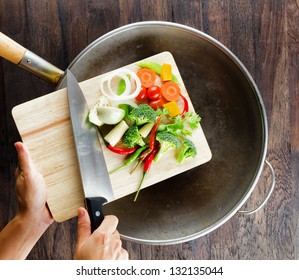 Fresh vegetables on the cutting board are falling in the wok. Concept of cooking.