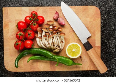 fresh vegetables on the cutting board and knife : garlic, cherry tomatoes, hot pepper, armillaria honey fungus , lemons.  - Powered by Shutterstock