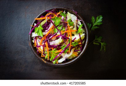 Fresh vegetables salad with purple cabbage, white cabbage,  lettuce, carrot in dark clay bowl on black background. Top view - Powered by Shutterstock