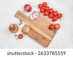Fresh vegetables and spices on a wooden cutting board ready for cooking on a light background, top view.