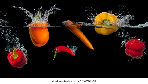 Fresh vegetables splashing in water on black background