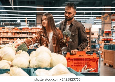 Fresh vegetables. Young couple are in supermarket together. - Powered by Shutterstock