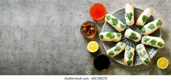 Fresh Vietnamese, Asian, Chinese food frame on grey concrete background. Spring rolls rice paper, lettuce, salad, vermicelli, noodles, shrimps, fish sauce, sweet chili, soy, lemon. Top view