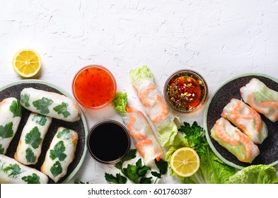 Fresh Vietnamese, Asian, Chinese food frame on white concrete background. Spring rolls rice paper, lettuce, salad, vermicelli, noodles, shrimps, fish sauce, sweet chili, soy, lemon. Top view.