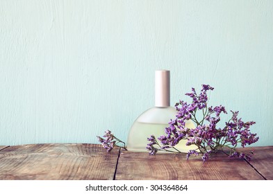 fresh vintage perfume bottle next to aromatic flowers on wooden table. retro filtered image