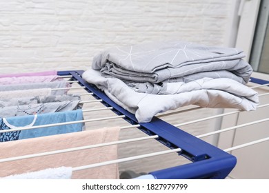 Fresh Washed Bed Linen Stacked, Piled On A Dryer, Dry Apparel On A Folding Portable Dryer Close Up, Housekeeping, Homework And Chores Concept.