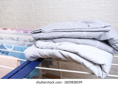 Fresh Washed Bed Linen Stacked, Piled On A Dryer, Dry Apparel On A Folding Portable Dryer Close Up, Housekeeping, Homework And Chores Concept.