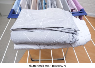 Fresh Washed Bed Linen Stacked, Piled On A Dryer, Dry Apparel On A Folding Portable Dryer Close Up, Housekeeping, Homework And Chores Concept.