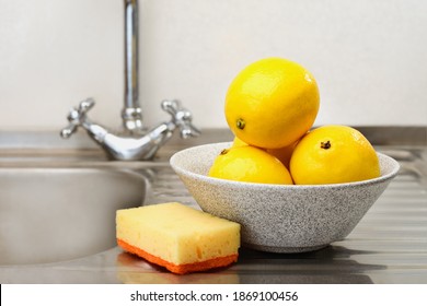 Fresh washed lemons in a bowl and a sponge for washing on the kitchen sink.