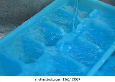 Fresh Water Filling Ice Cube Trays For Freezing. Trays Are In A Sink And The Top Tray Is Overflowing Into The Bottom Tray. 