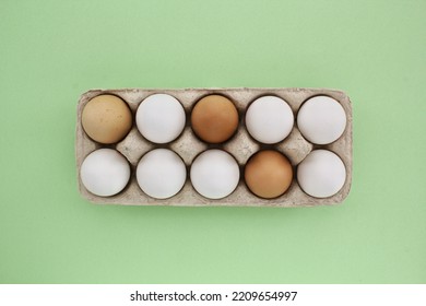 Fresh White And Brown Chicken Eggs In Carton Paper Box On Green Background. Natural Healthy Nutrition Organic Farm Food Product Concept. World Egg Day, Easter Holiday Composition. Copy Space, Flatlay