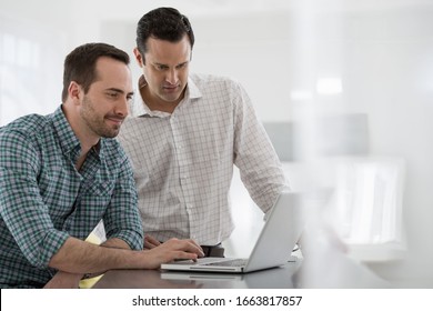 A fresh white building interior, flooded with light. Two men standing at a table using a laptop computer. - Shutterstock ID 1663817857