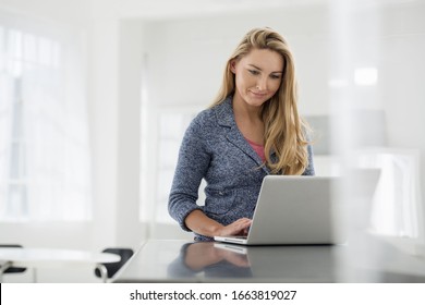 A fresh white building interior, flooded with light. A woman sitting at a table using a digital tablet. - Shutterstock ID 1663819027