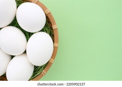 Fresh White Chicken Eggs In Wooden Rattan Wicker Basket On Green Background. Natural Healthy Nutrition Organic Farm Food Product Concept. World Egg Day, Easter Holiday Composition. Close-up, Flatlay