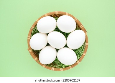 Fresh White Chicken Eggs In Wooden Rattan Wicker Basket On Green Background. Natural Healthy Nutrition Organic Farm Food Product Concept. World Egg Day, Easter Holiday Composition. Close-up, Flatlay