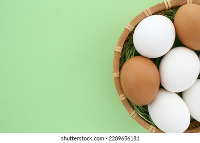 Fresh White Chicken Eggs In Wooden Rattan Wicker Basket On Green Background. Natural Healthy Nutrition Organic Farm Food Product Concept. World Egg Day, Easter Holiday Composition. Close-up, Flatlay