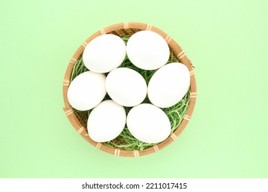 Fresh White Chicken Eggs In Wooden Rattan Wicker Basket On Green Background. Natural Healthy Nutrition Organic Farm Food Product Concept. World Egg Day, Easter Holiday Composition. Close-up, Flatlay