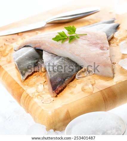Fresh white fish fillets displayed on chopping board with crushed ice, knife, cracked rock salt and parsley garnish 