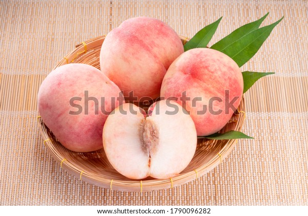 Fresh White Peach\
fruits with leaves on bamboo mat, Korean white peach in Bamboo\
basket on wooden bamboo\
table.