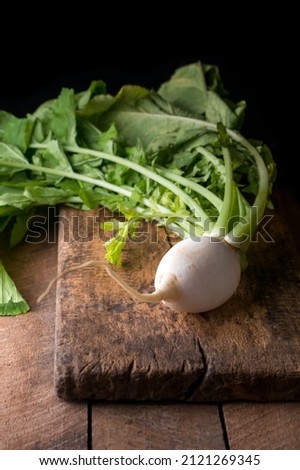 fresh white radish with leaves, edible and healthy root vegetable on a wooden board, dark background with copy space, rustic concept