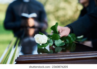 Raza blanca fresca puesta por una mujer con atuendo de luto sobre una tapa de ataúd cerrada contra un sacerdote con Biblia abierta realizando el servicio funerario