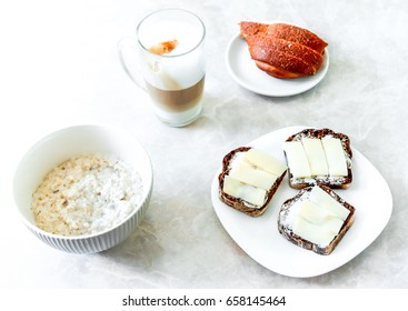 fresh white still life with coffee, white bred on small plate, sandwidges and porridge against light table background. White breakfast. Background white breakfast elements