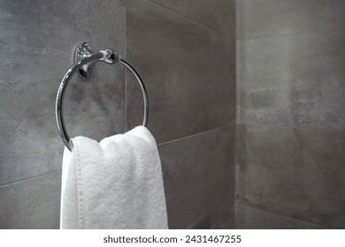 A fresh white towel hangs on a sleek metal towel ring on an elegant gray tiled bathroom wall. - Powered by Shutterstock