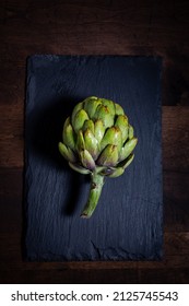 Fresh Whole Artichoke On Dark Slate Serving Board On Butcher Block Texture￼