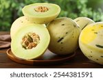 Fresh whole and cut honeydew melons on wooden table against blurred green background, closeup