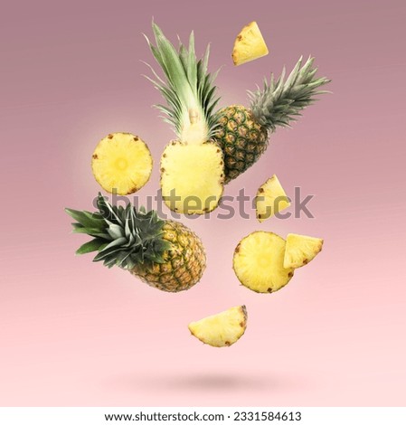 Fresh whole and cut pineapples falling on pale pink background
