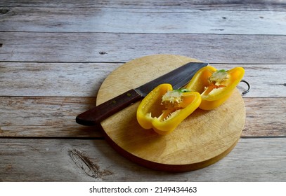 Fresh yellow bell peppers (capsicum) has been cut with a knife and a wood chopping block isolated on wooden background. Concept for health and vitamins.