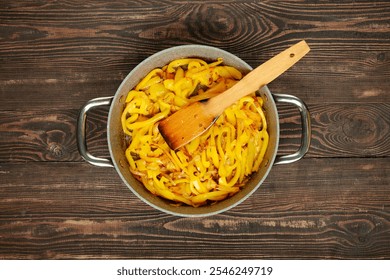 Fresh yellow peppers are being sauteed in a pan with a wooden spatula, showcasing vibrant colors and cooking techniques. The wooden countertop adds a rustic touch to this kitchen activity. - Powered by Shutterstock