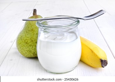 fresh yoghurt in a glass in front of a pear and a bananas