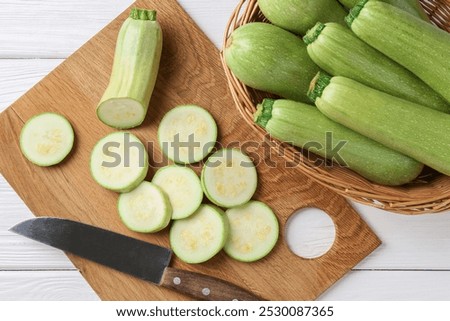 Fresh zucchinis and knife on white wooden table, flat lay