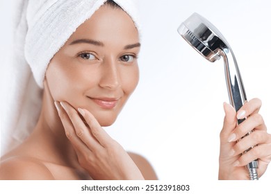 A fresh-faced woman with glowing skin and towel-wrapped hair smiles while holding a shower head, showcasing a clean and rejuvenating skincare routine. Ideal for wellness, beauty, and self-care - Powered by Shutterstock