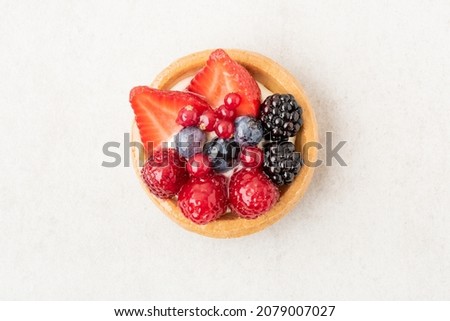 Freshly backed tartlet with strawberries, blueberries, raspberries on beige stone background. Top view, flat lay of food photography minimal concept.