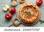 A freshly baked apple tart sits on a rustic wooden board, garnished with almonds and mint, accompanied by red apples and a small bowl of honey, inviting a cozy atmosphere.